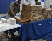 Two men, standing near pizza boxes in a gymnasium